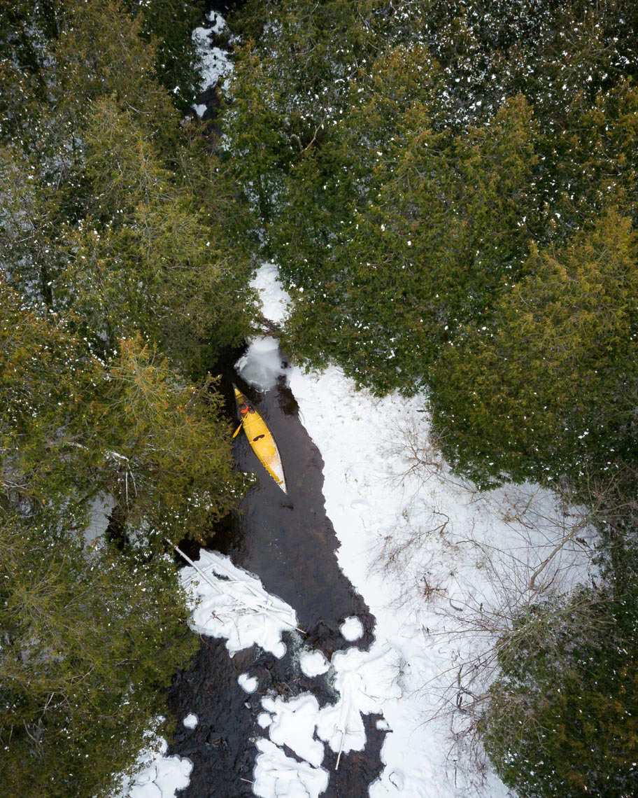Aerial view of person paddling kayak through Eramosa river and Rockwood forest in winter 