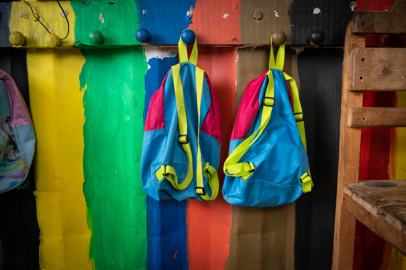 Two children backpacks hanging against a colourful wooden wall