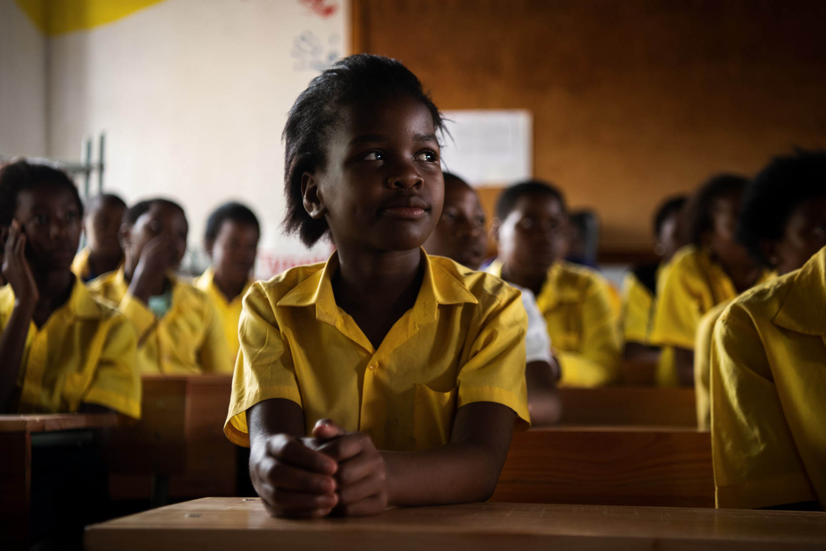 An African school girl in uniform looks on with classmates behind her in South Africa