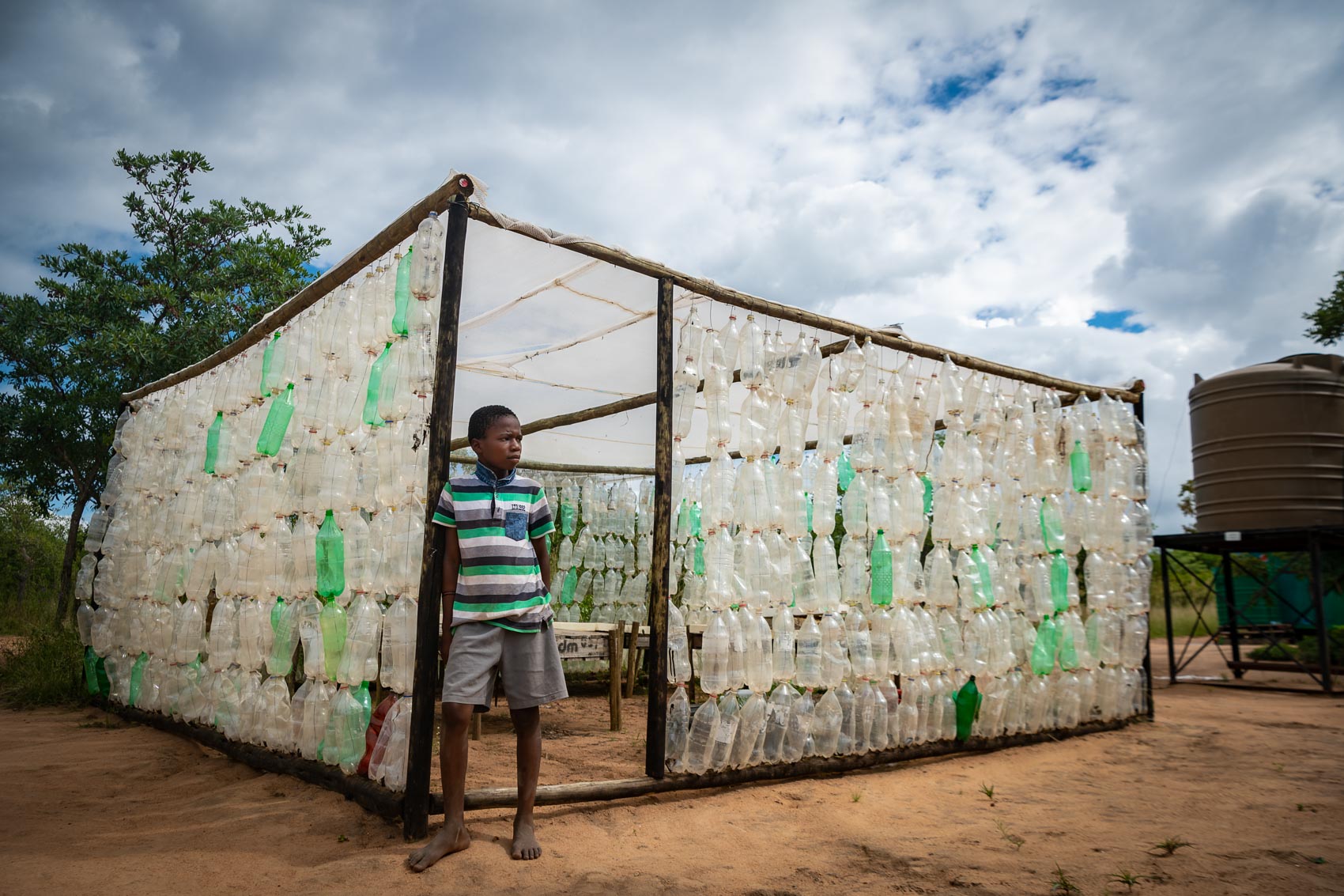 An African boy leaning against a wooden structure made from recycled bottles at Nourish NPO