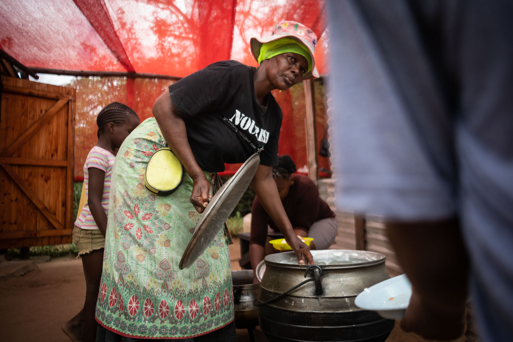 A granny worker at Nourish NPO opening the lid of a pot filled with porridge